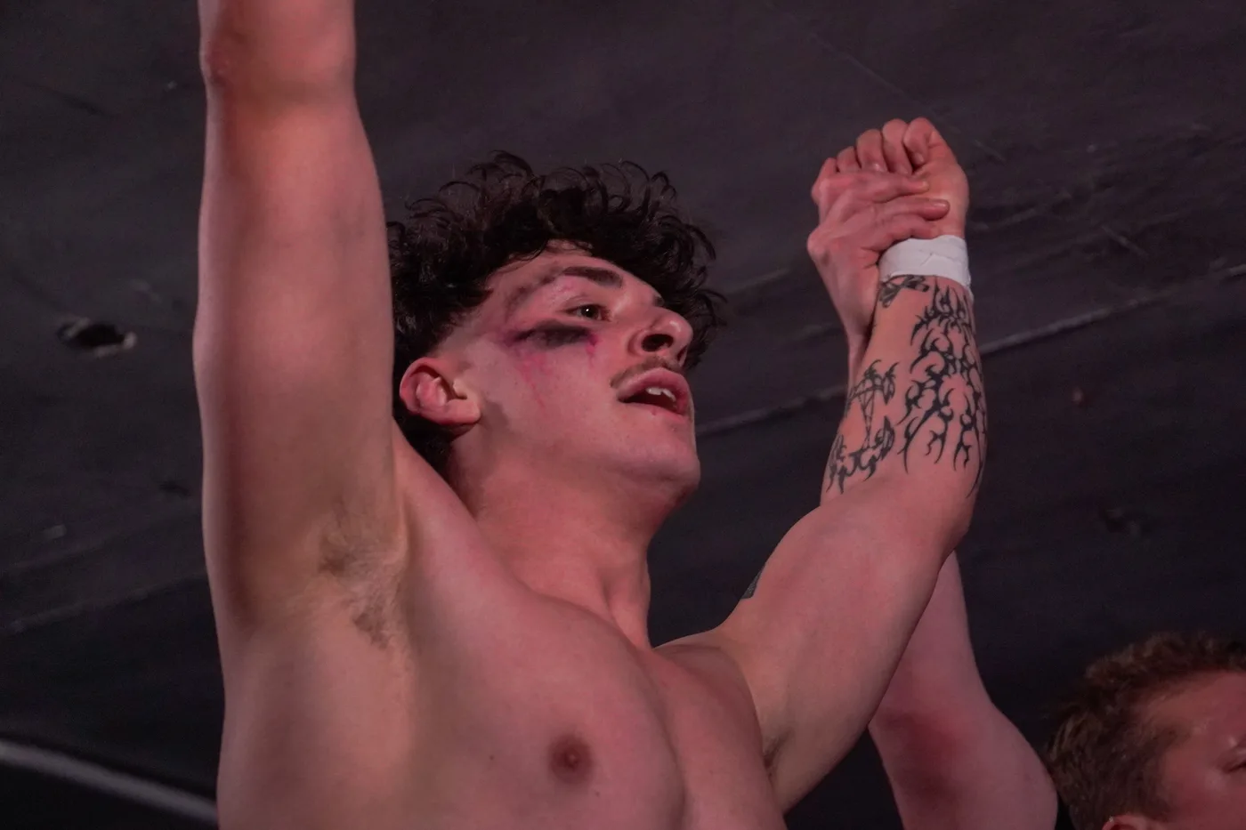 A wrestler with a tattooed arm celebrating a win in the EVO ring
