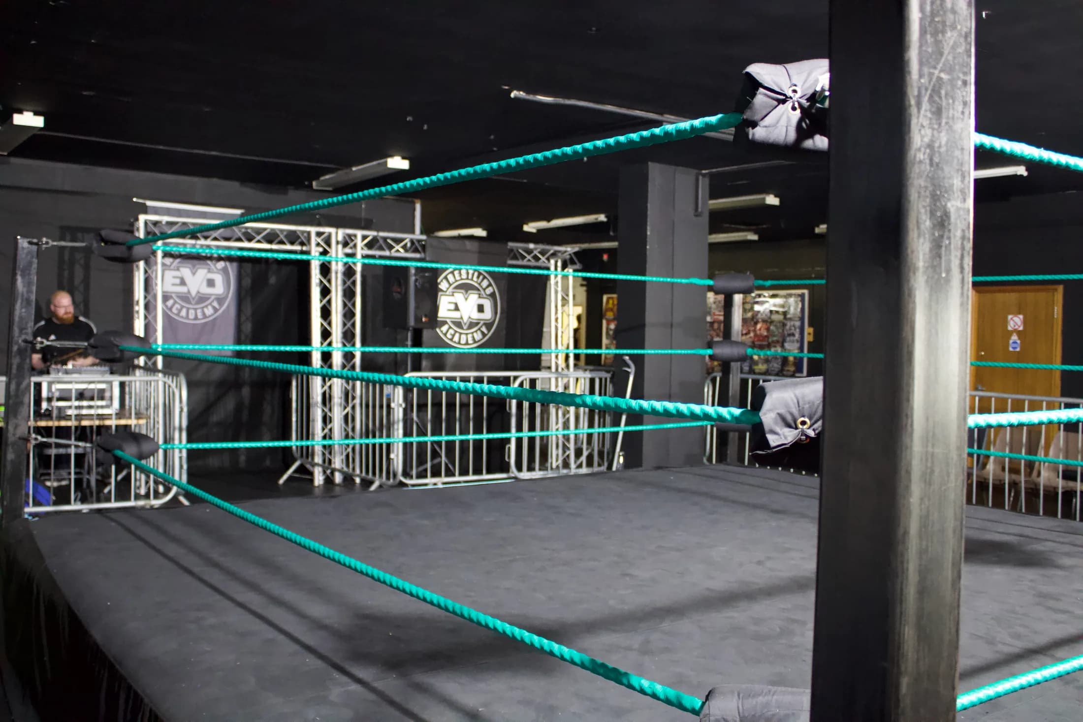 A wide view of the EVO wrestling ring, turquoise ropes and academy banners